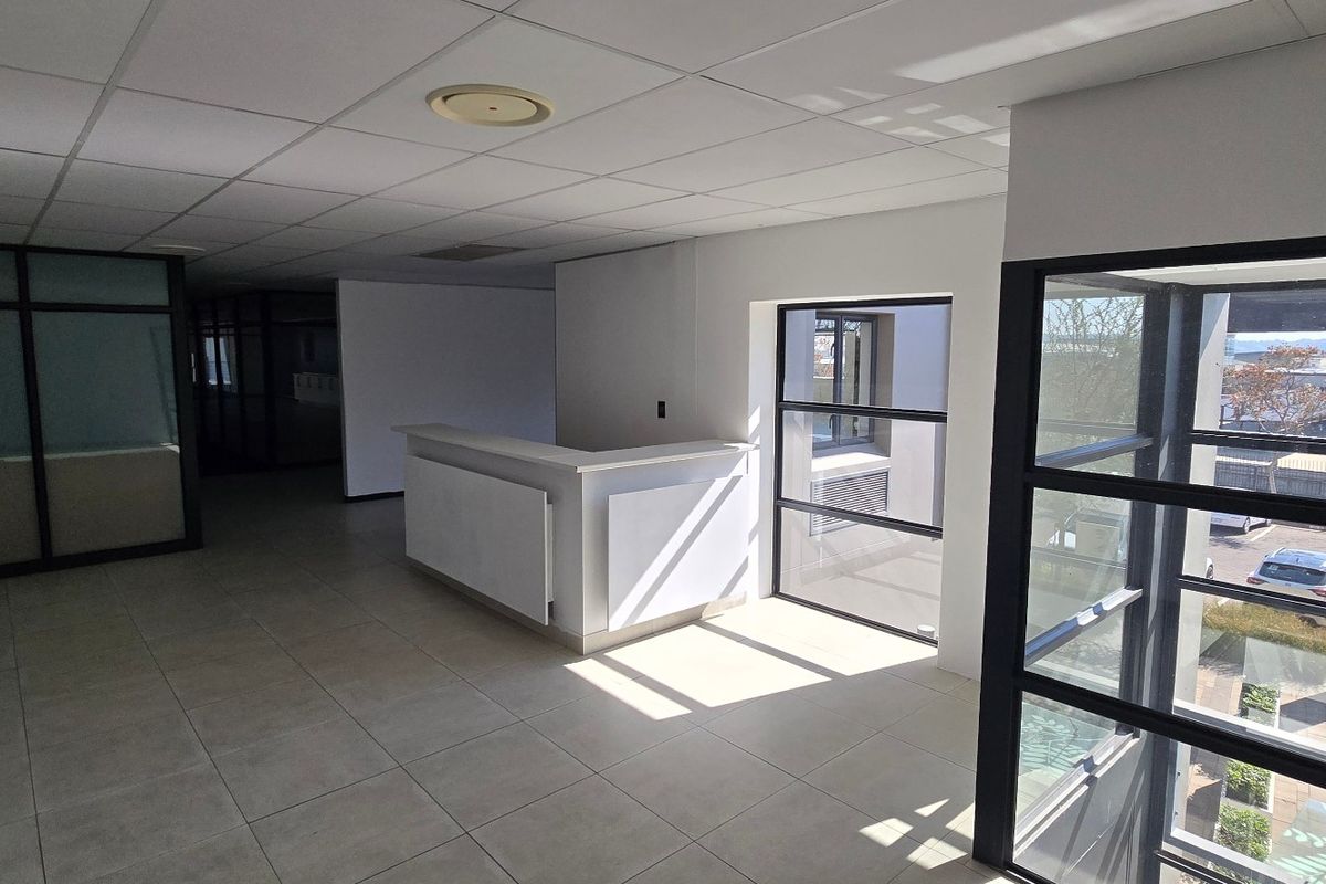 Open-plan commercial office space featuring a built-in reception desk, tiled flooring, suspended ceiling, and large windows with natural light.