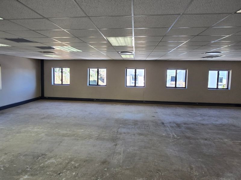 A large, open-plan commercial office space featuring a suspended ceiling, recessed lighting, and multiple windows, currently awaiting flooring installation and final finishes.