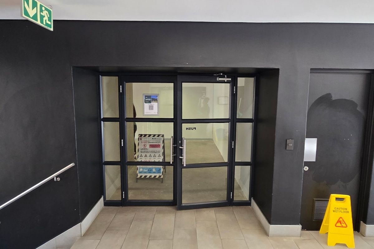 Commercial building entrance featuring glass double doors, tiled flooring, and a stainless steel handrail, with adjacent restroom access.