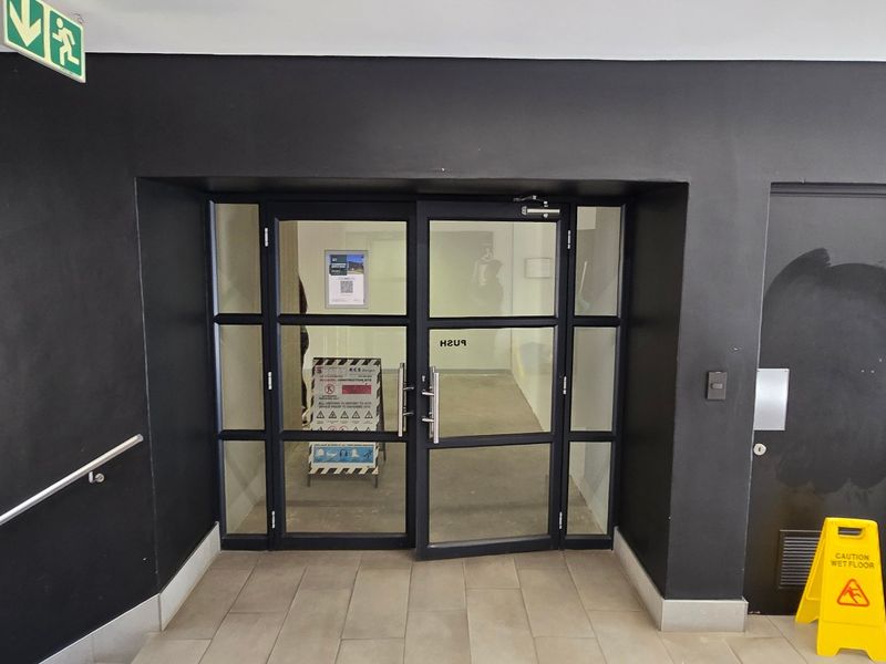 Commercial building entrance featuring glass double doors, tiled flooring, and a stainless steel handrail, with adjacent restroom access.