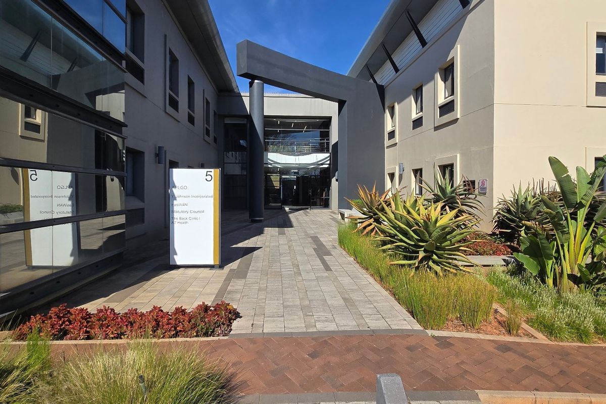 Modern commercial office building entrance featuring a paved walkway, glass facade, and professional landscaping.