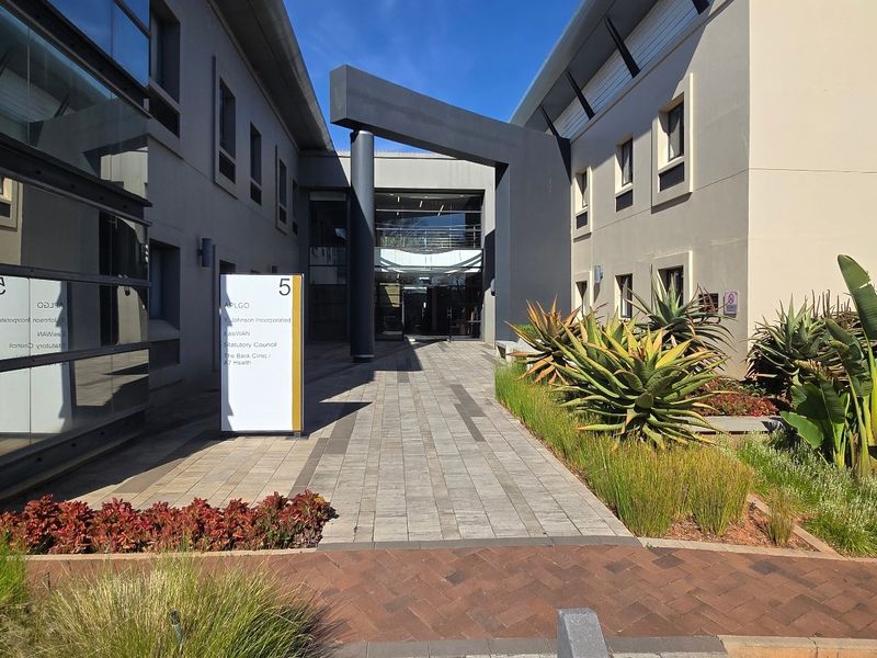 Modern commercial office building entrance featuring a paved walkway, glass facade, and professional landscaping.