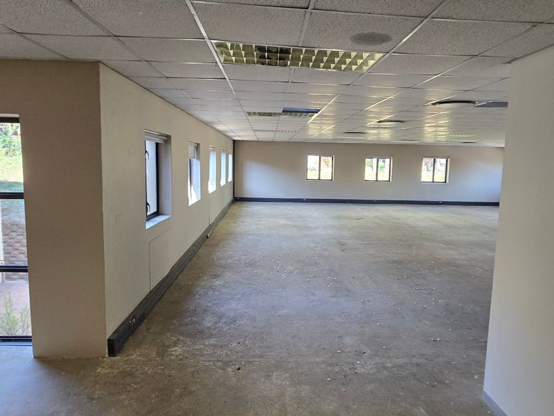 A large, open-plan commercial office space featuring a suspended ceiling, recessed lighting, and multiple windows providing natural light.