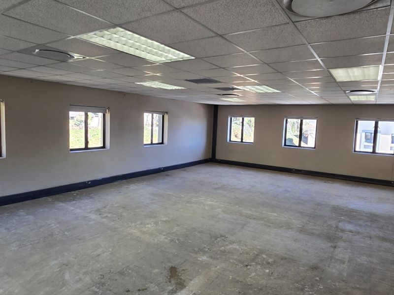 A spacious, vacant commercial office area featuring a suspended ceiling with recessed lighting, multiple windows, and unfinished concrete flooring ready for final finishes.