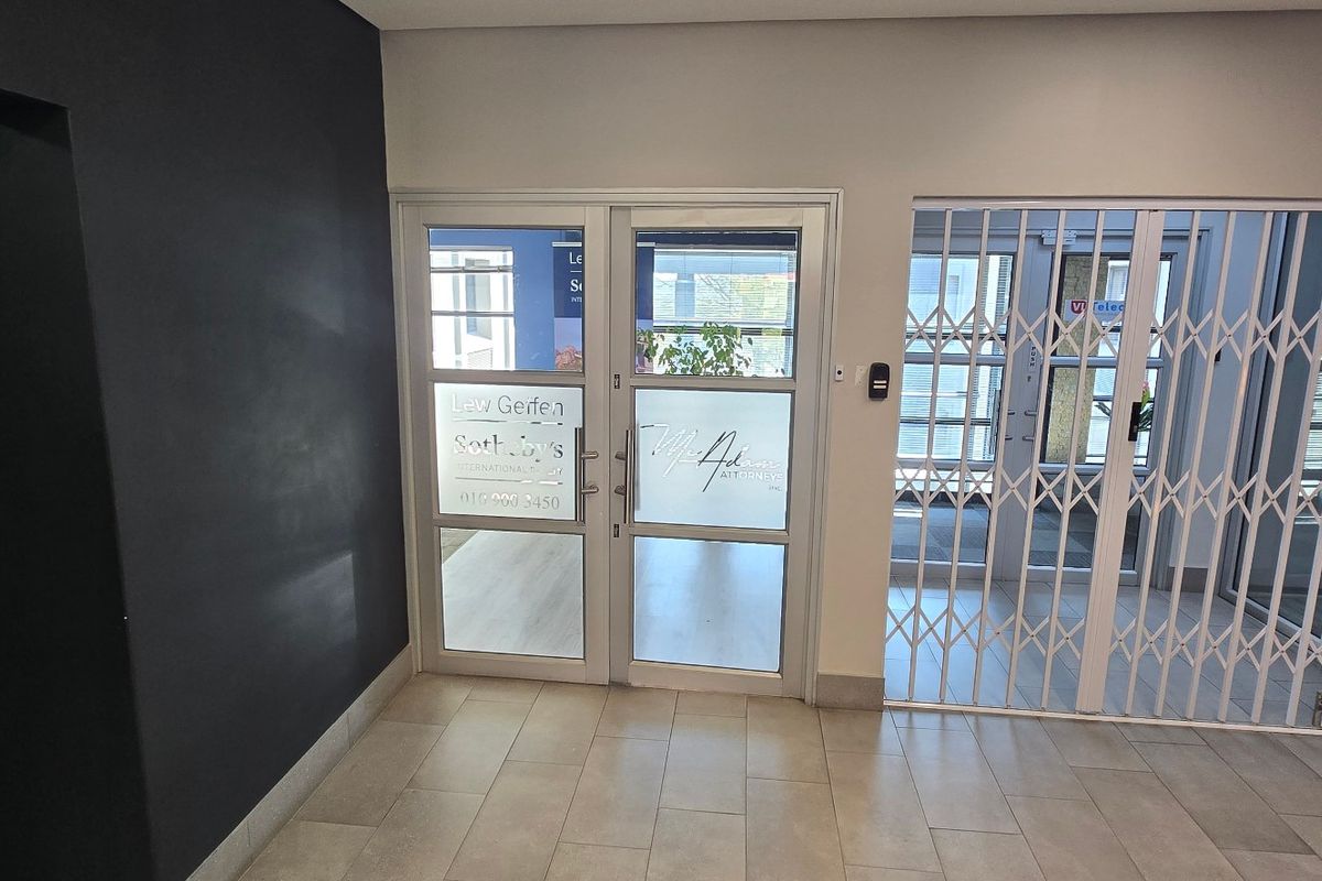 A clean and professional commercial entrance area featuring tiled flooring, a secure glass door, and a white security gate.