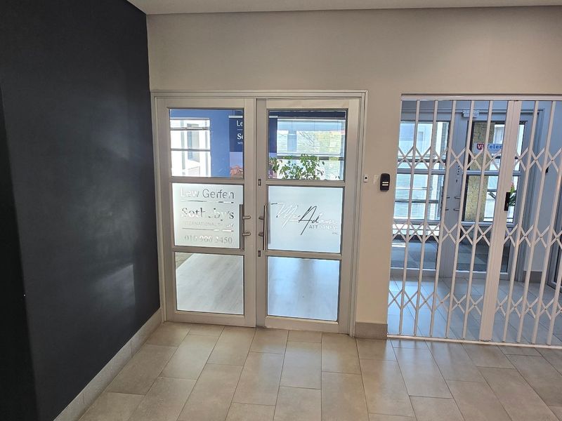 A clean and professional commercial entrance area featuring tiled flooring, a secure glass door, and a white security gate.