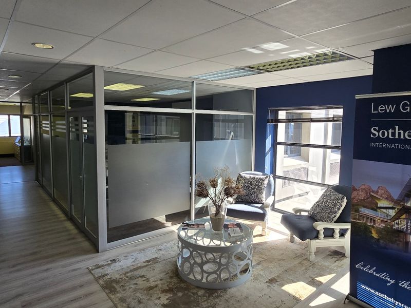 A professional commercial office space featuring glass partitions, suspended ceilings, and laminate flooring, providing a bright and functional work environment.