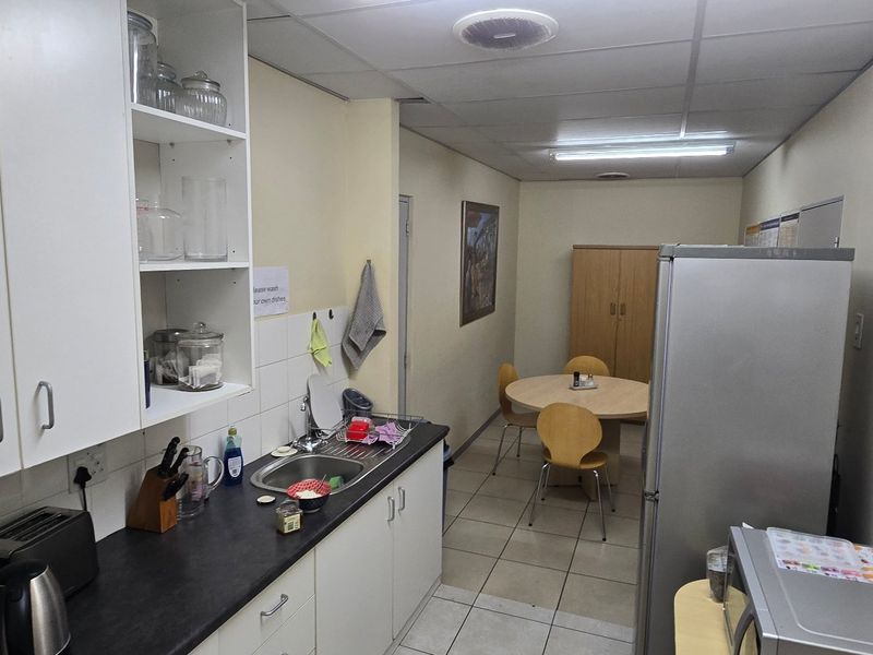 A functional commercial kitchen space featuring built-in cabinetry, a stainless steel sink, and tiled flooring, suitable for staff breakroom or office utility use.