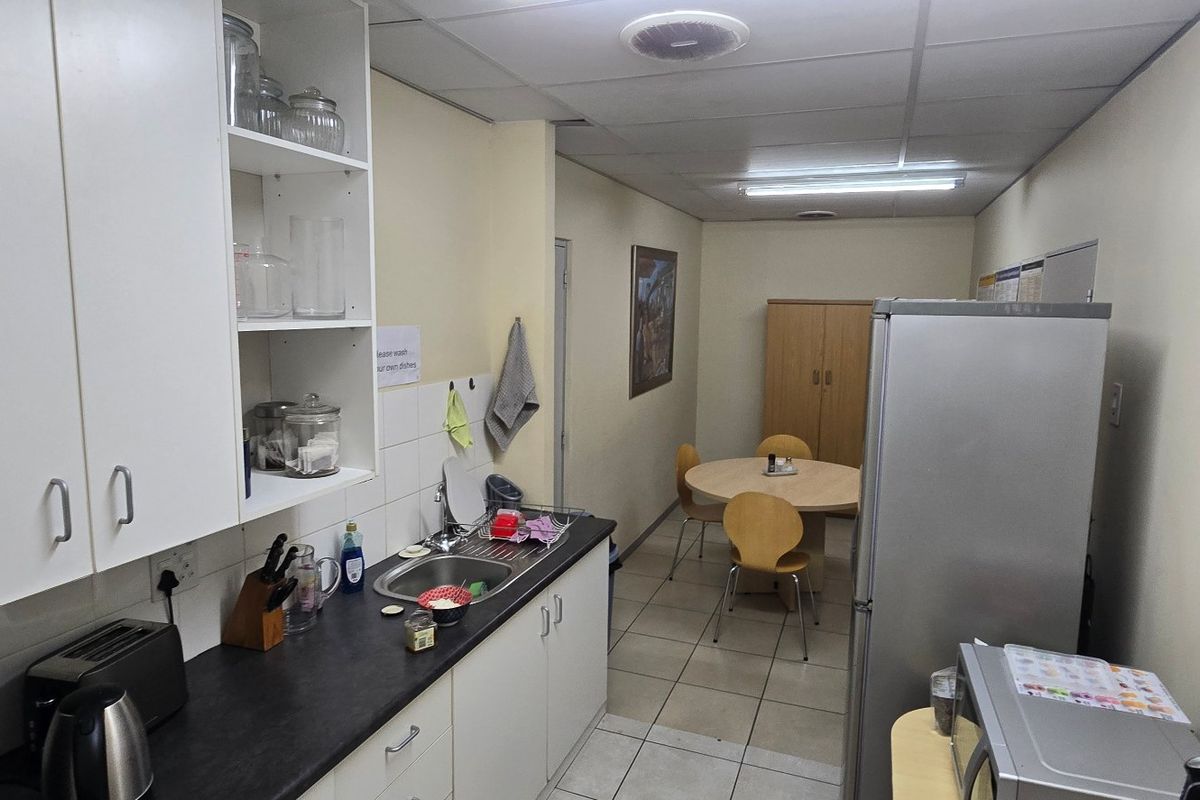 A functional commercial kitchen space featuring built-in cabinetry, a stainless steel sink, and tiled flooring, suitable for staff breakroom or office utility use.