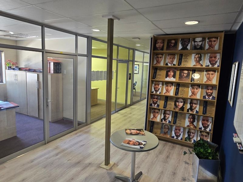 A commercial office space featuring glass partition walls, laminate flooring, and a suspended ceiling with recessed lighting.