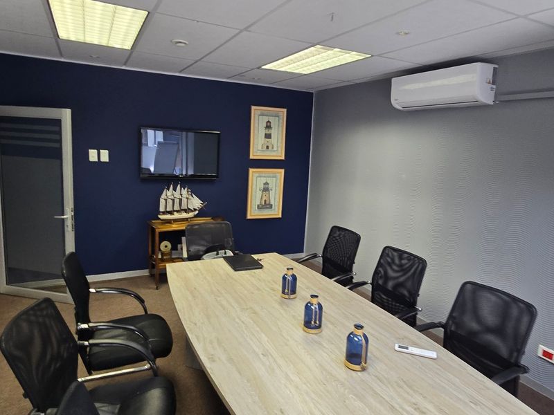 A professional office meeting room featuring a glass partition wall, suspended ceiling with recessed lighting, and a wall-mounted air conditioning unit.