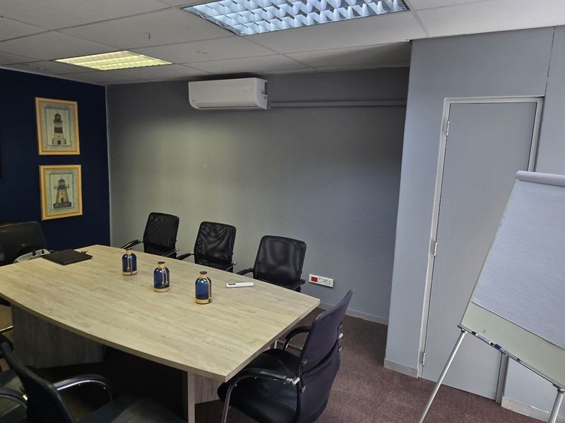 A functional office meeting room featuring a suspended ceiling, recessed lighting, split-system air conditioning, and carpeted flooring.