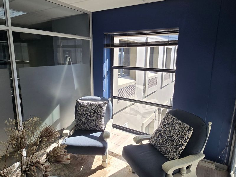 A bright office space featuring glass partition walls, large windows with aluminium frames, and a modern blue accent wall.