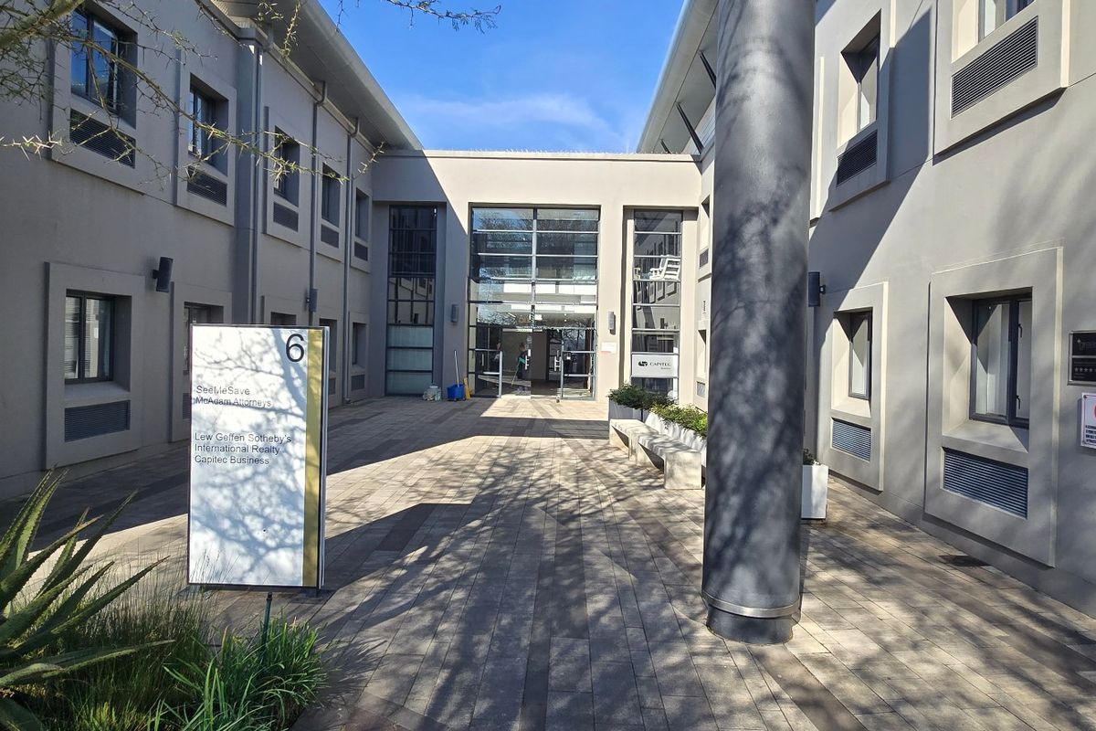 A modern commercial office building entrance featuring a paved courtyard, glass facade, and professional signage.