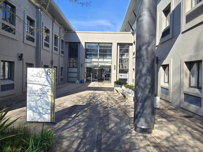 A modern commercial office building entrance featuring a paved courtyard, glass facade, and professional signage.