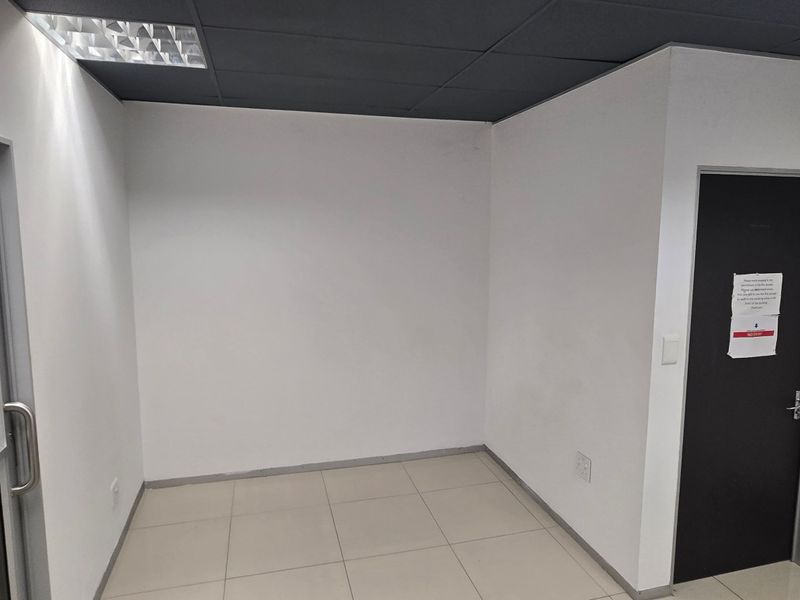 A clean, empty commercial office space featuring neutral tiled flooring, a dark suspended ceiling with recessed lighting, and modern door fixtures.