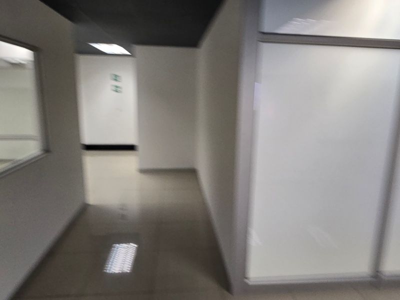 A commercial hallway featuring tiled flooring, recessed ceiling lighting, and glass partition walls.