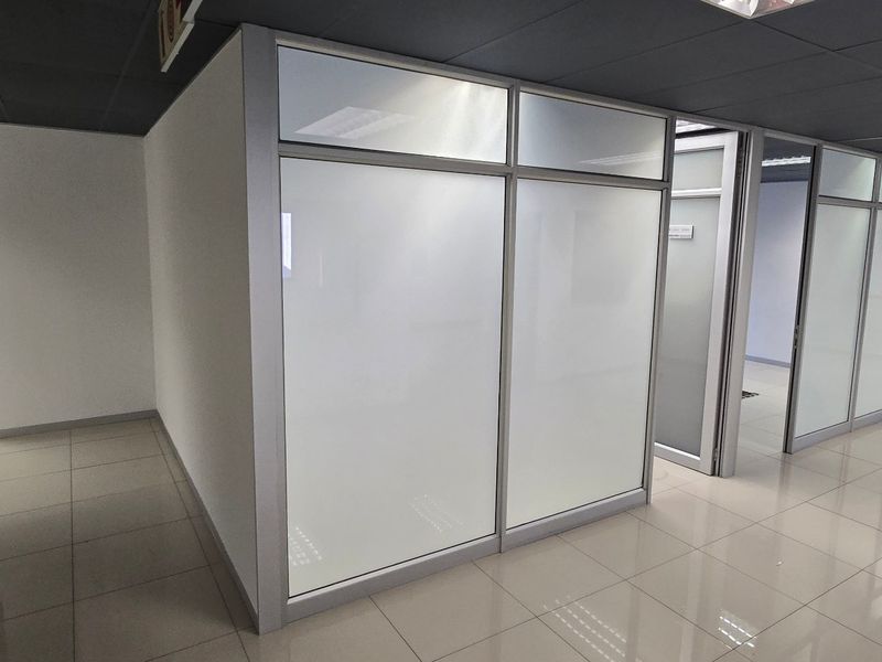 Modern commercial office space featuring clean tiled flooring, suspended ceilings, and professional frosted glass partitioning for private work areas.