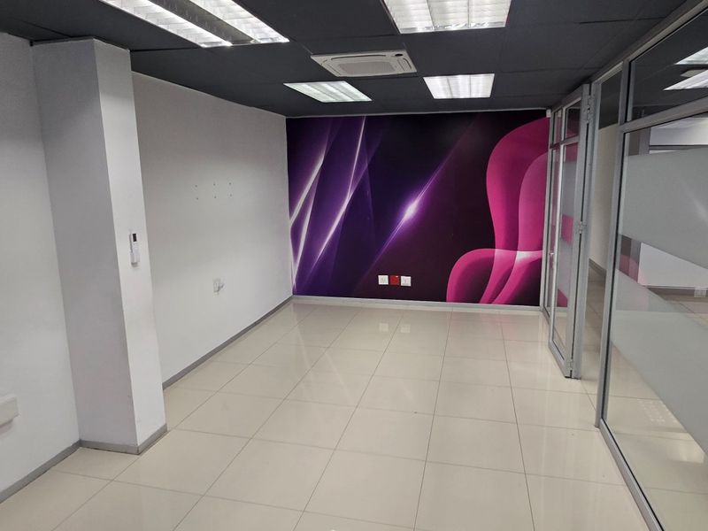 A modern, empty commercial office space featuring tiled flooring, glass partitions, and recessed ceiling lighting with a decorative feature wall.