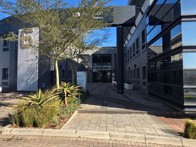 Modern commercial office building entrance featuring a paved walkway, glass facade, and contemporary architectural design elements.