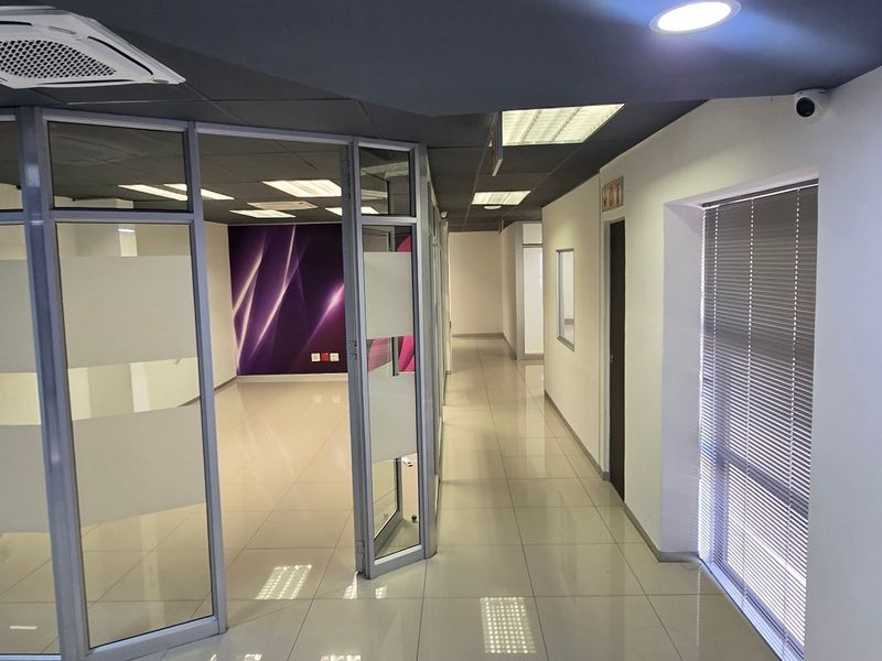 Modern commercial office space featuring glass partitions, tiled flooring, recessed lighting, and integrated ceiling air conditioning, providing a clean and professional work environment.