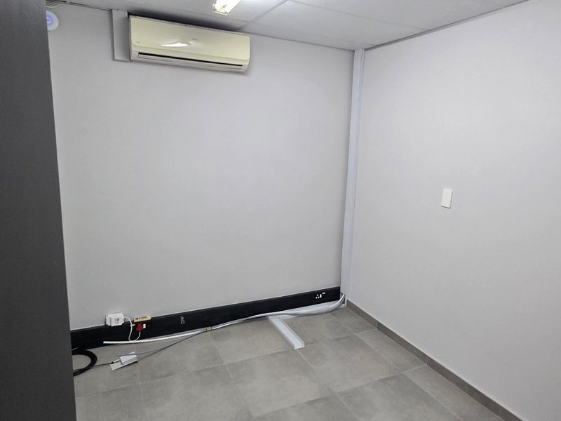 A clean, empty office space featuring tiled flooring, a suspended ceiling, and a wall-mounted split-system air conditioning unit.