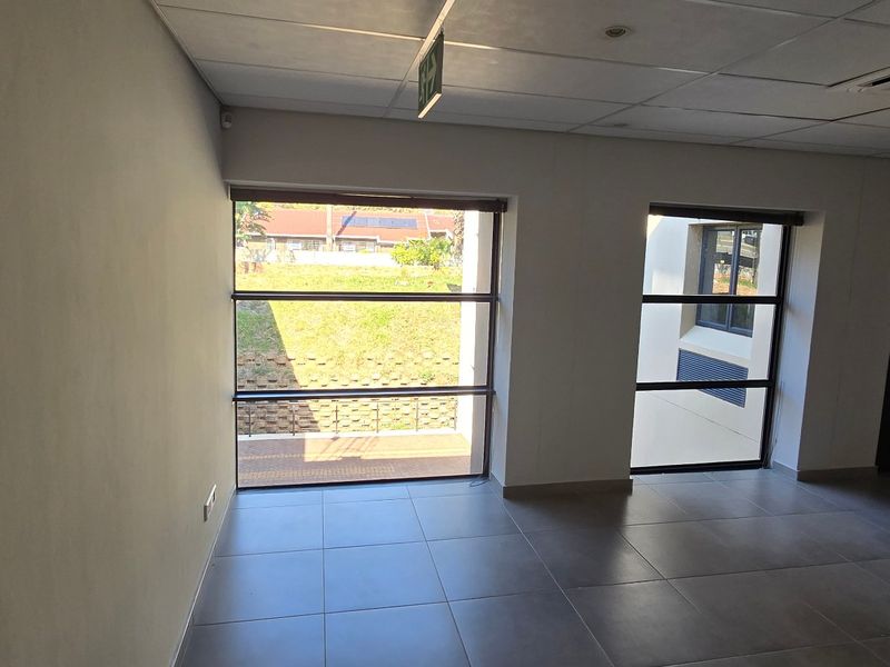 A bright, empty commercial office space featuring tiled flooring, a suspended ceiling with recessed lighting, and large windows providing natural light.