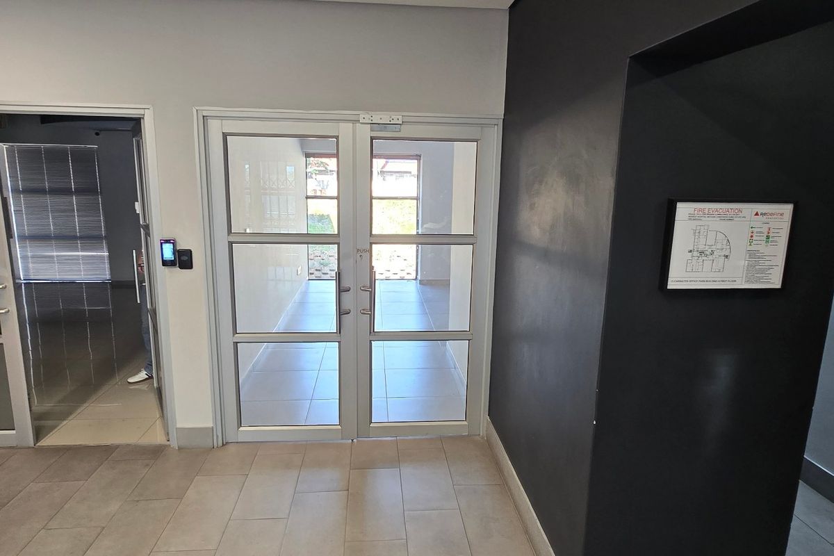 A clean commercial hallway featuring tiled flooring, aluminium framed glass doors, and an integrated access control system.