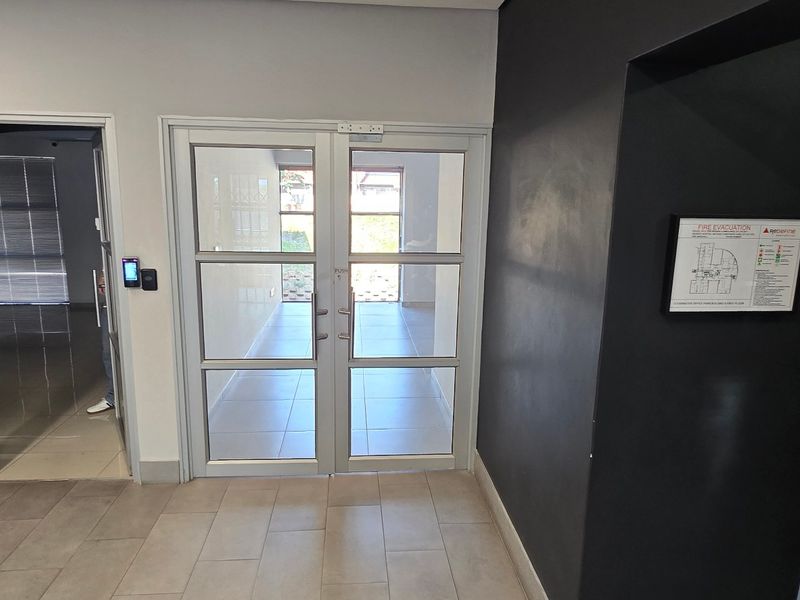 A clean commercial hallway featuring tiled flooring, aluminium framed glass doors, and an integrated access control system.