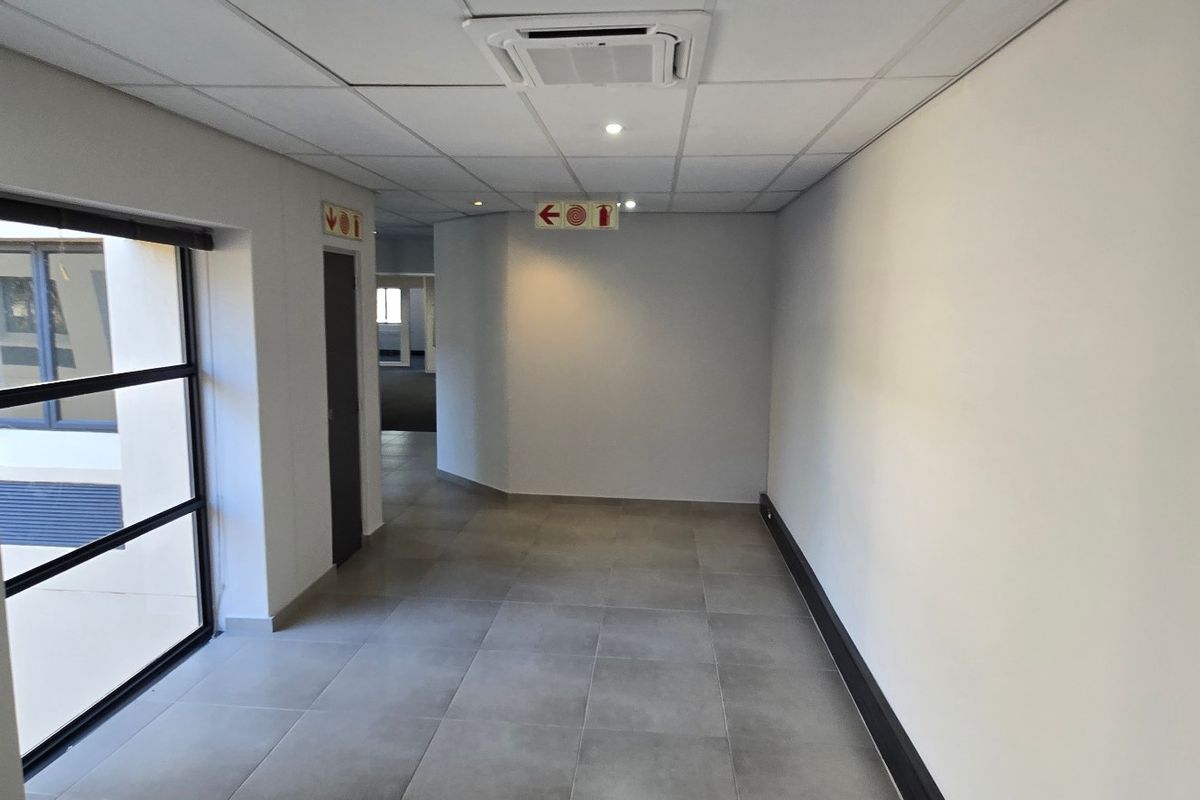 A clean, modern commercial hallway featuring tiled flooring, a suspended ceiling with recessed lighting, and ducted air conditioning.