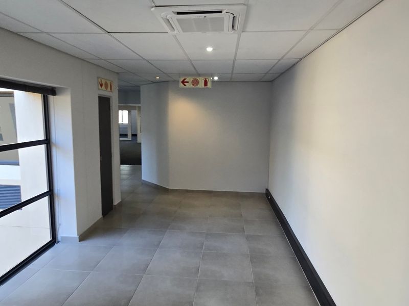 A clean, modern commercial hallway featuring tiled flooring, a suspended ceiling with recessed lighting, and ducted air conditioning.