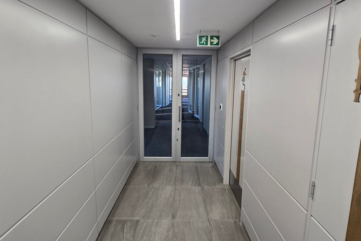 A modern, well-maintained commercial hallway featuring clean wall paneling, tiled flooring, and glass double doors leading to an adjacent office space.