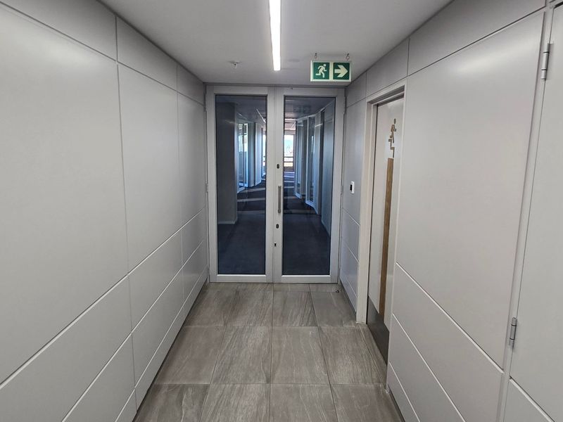 A modern, well-maintained commercial hallway featuring clean wall paneling, tiled flooring, and glass double doors leading to an adjacent office space.