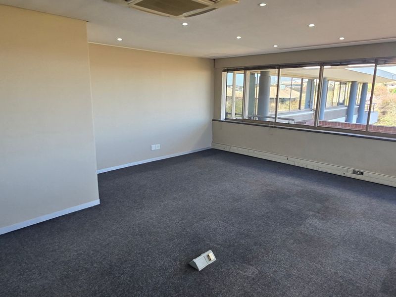A spacious, empty commercial office featuring large windows, recessed lighting, carpeted flooring, and integrated air conditioning units.