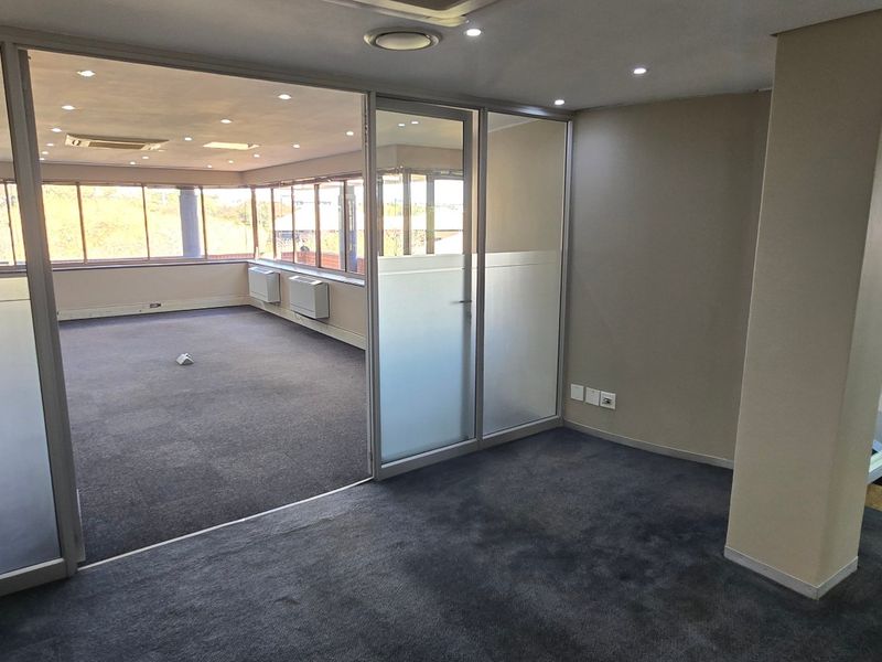 A bright, open-plan office space featuring glass partitions, recessed lighting, and carpeted flooring, offering a professional and versatile commercial work environment.