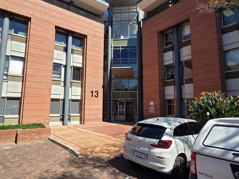 Front elevation of a commercial office building featuring a brick facade, glass entrance atrium, and paved driveway access.