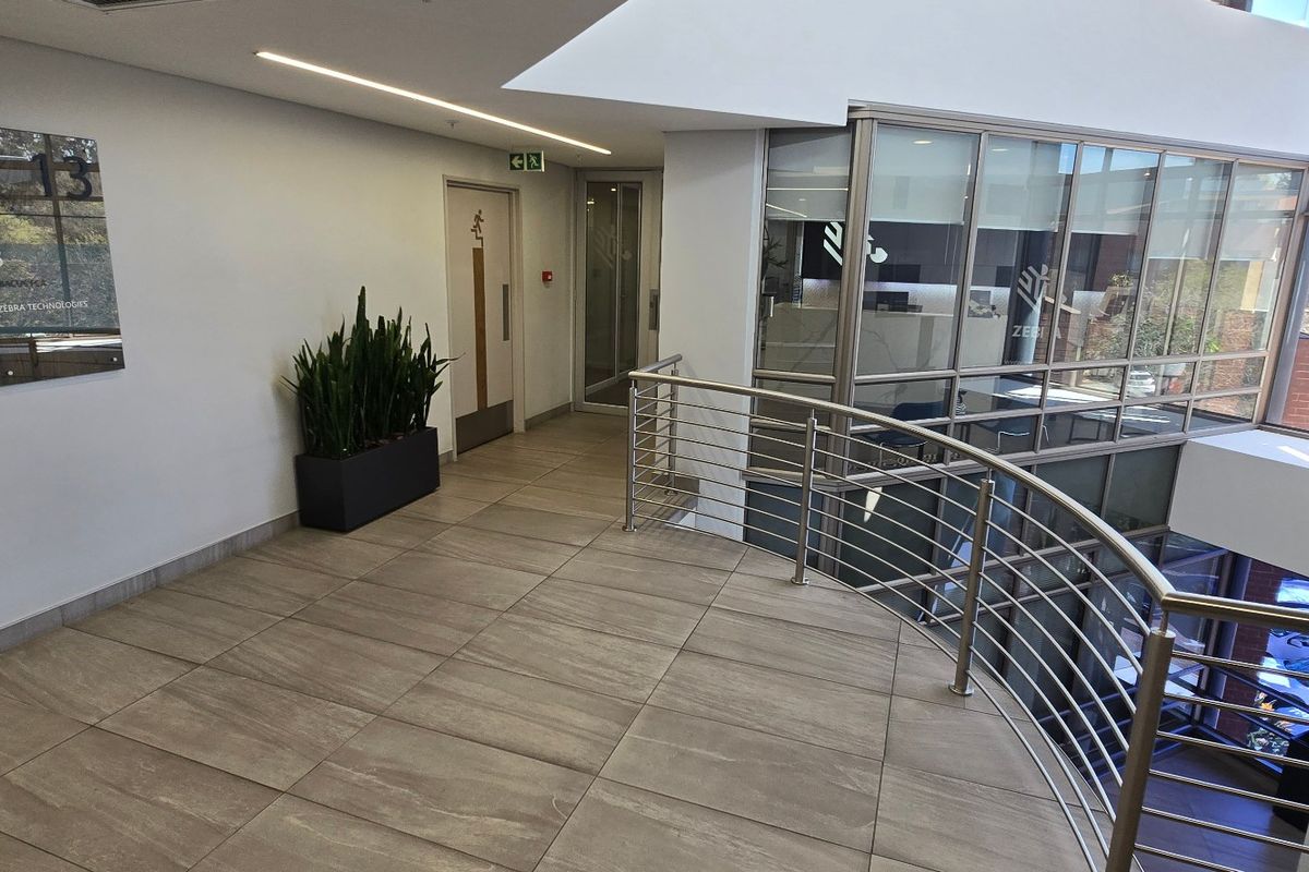Modern commercial hallway featuring tiled flooring, a sleek stainless steel balustrade, and glass partitioning overlooking the lower level.