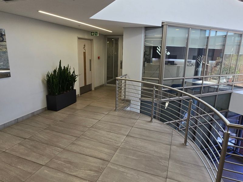 Modern commercial hallway featuring tiled flooring, a sleek stainless steel balustrade, and glass partitioning overlooking the lower level.