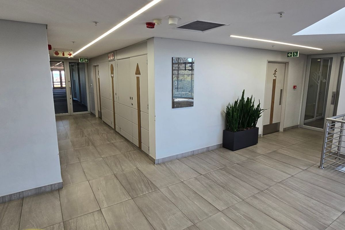 A clean, modern commercial hallway featuring tiled flooring, recessed linear lighting, and stainless steel handrails, providing access to various office or service areas.