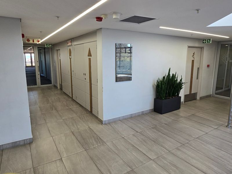 A clean, modern commercial hallway featuring tiled flooring, recessed linear lighting, and stainless steel handrails, providing access to various office or service areas.
