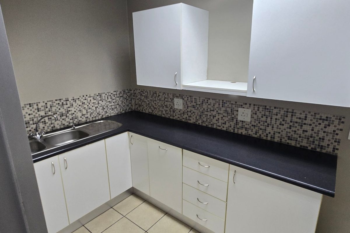 A compact kitchenette featuring white cabinetry, dark laminate countertops, a stainless steel sink, and a decorative mosaic tile backsplash.