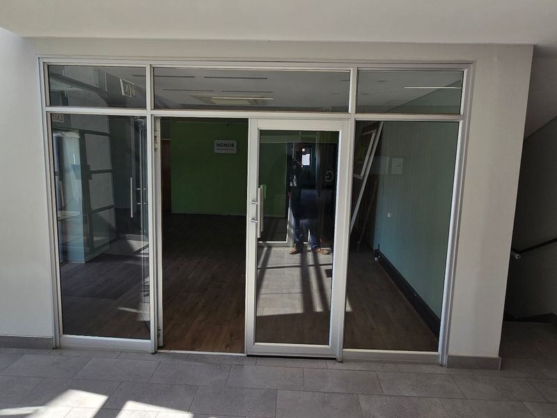 Modern commercial office entrance featuring aluminium framed glass doors and partitioning, leading into an open-plan workspace with wood-look flooring.