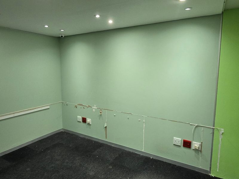 An empty office space featuring recessed ceiling lighting, carpet flooring, and a glass door entrance, currently showing signs of wall surface wear.