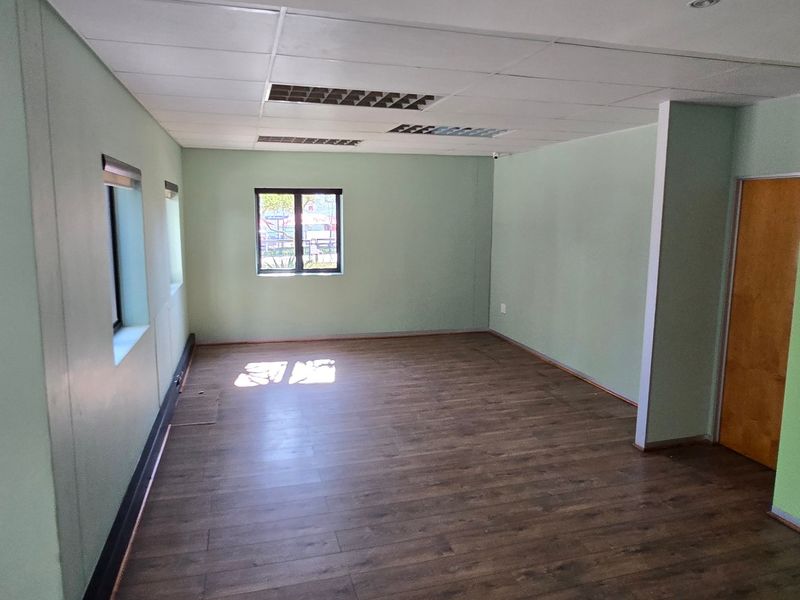 A vacant commercial office space featuring laminate flooring, recessed ceiling lights, and a neutral color palette, suitable for a variety of business configurations.