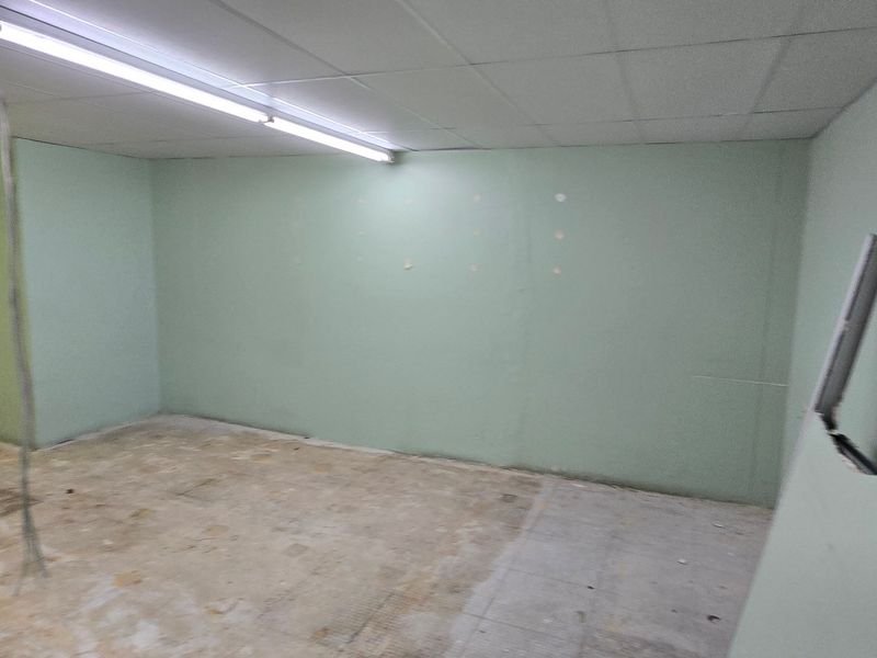 An empty commercial office space featuring a suspended ceiling, fluorescent lighting, and unfinished wall and floor surfaces, ready for renovation.