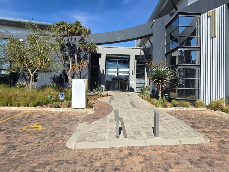 Modern commercial office building entrance featuring a paved driveway, accessible parking, and contemporary glass and metal facade architecture.