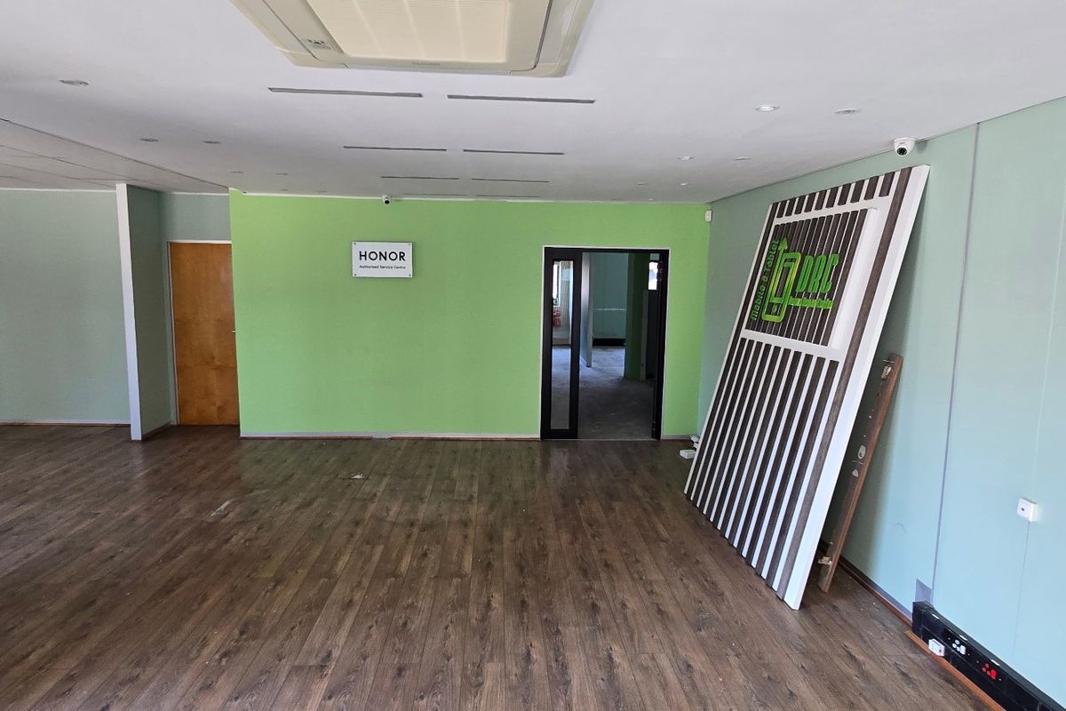 An open-plan commercial office space featuring laminate wood flooring, recessed ceiling lighting, and a ceiling-mounted air conditioning unit.
