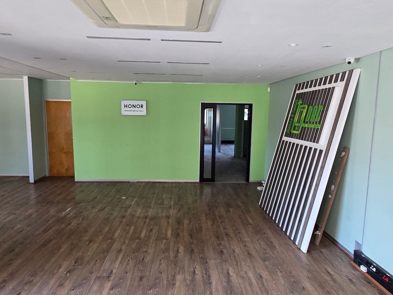 An open-plan commercial office space featuring laminate wood flooring, recessed ceiling lighting, and a ceiling-mounted air conditioning unit.