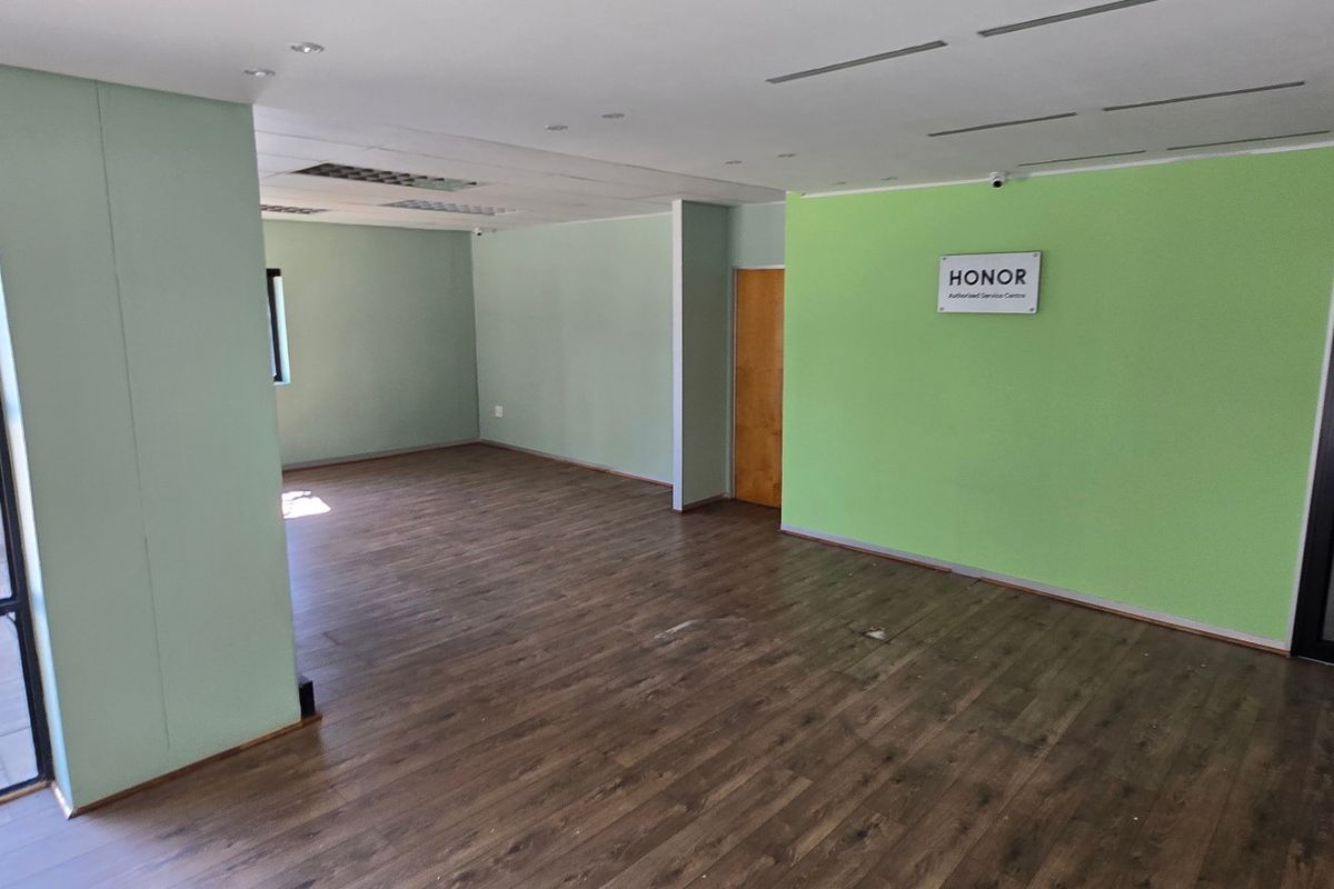 An open-plan commercial office space featuring laminate flooring, recessed ceiling lighting, and large windows, providing a versatile layout for business operations.