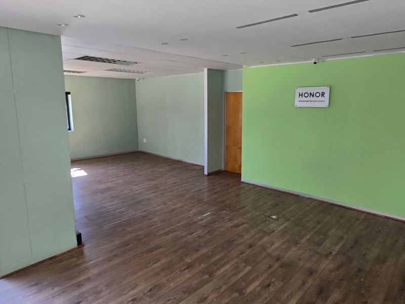 An open-plan commercial office space featuring laminate flooring, recessed ceiling lighting, and large windows, providing a versatile layout for business operations.